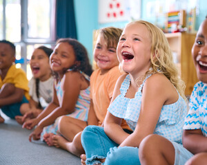 Line Of Smiling Primary Or Elementary School Students Sitting On Floor During Classroom Lesson