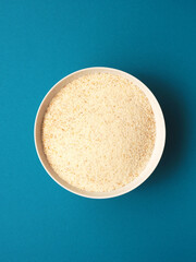 Organic wheat semolina in a white ceramic bowl on a blue studio background, healthy food or ingredients