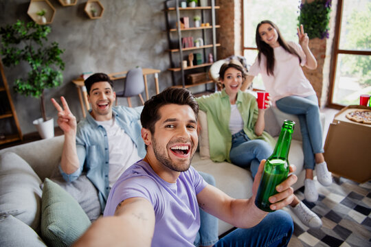 Photo of funky positive fellows sitting couch hold beer bottle cup make selfie shoe v-sign apartment indoors
