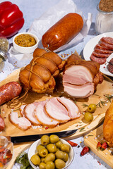 an abundance of meat delicacies on a concrete background surrounded by various spices and herbs, olives, peppers