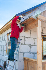 Fototapeta premium A worker builds a roof in a house while standing on a wooden ladder. Blue sky