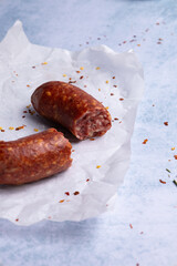 smoked spicy sausage with cheese on white paper surrounded by spices and herbs, on a light background