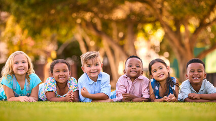 Portrait Of Multi-Cultural Primary Or Elementary School Student Friends Lying On Grass Outdoors - 763137134