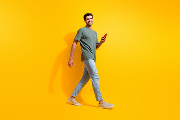 Fototapeta na wymiar Full length photo of cheerful good mood man dressed khaki t-shirt texting messages modern gadget isolated yellow color background