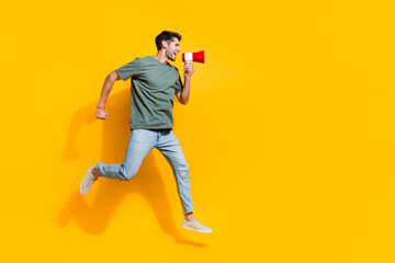 Fototapeta na wymiar Full length photo of excited cheerful guy wear khaki t-shirt jumping high screaming bullhorn empty space isolated yellow color background