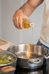 Black male hand pouring oil in a pot to cook a meat with vegetables, close up view