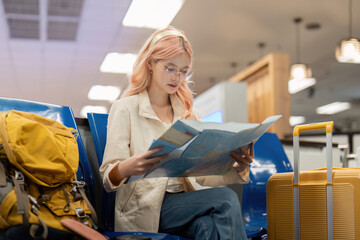 Happy young woman asian is sitting in airport near suitcase and reading map