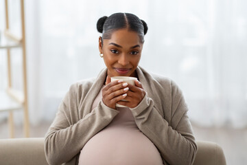 Portrait of cheerful young black pregnant woman drinking tea