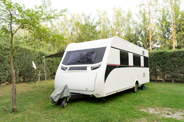 A white trailer,a motorhome for travel,a motorhome,camper,trailer without a car against a background of beautiful bushes stands on short green lawn grass.Technologies of transport, means of travel