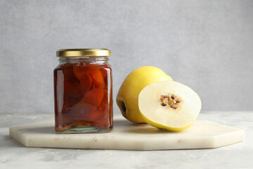 Tasty homemade quince jam in jar and fruits on grey textured table