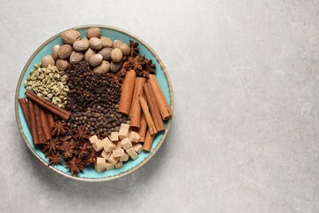 Different spices and nuts in bowl on light gray textured table, top view. Space for text