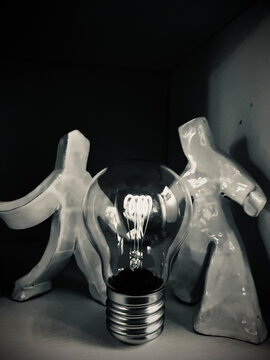 Foto concettuale di due omini in ceramica con al centro una lampadina 
