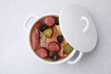 Meat solyanka soup with thin dry smoked sausages in pot on light table, top view