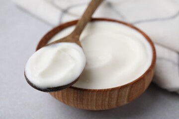 Delicious natural yogurt in bowl and spoon on light grey table, closeup