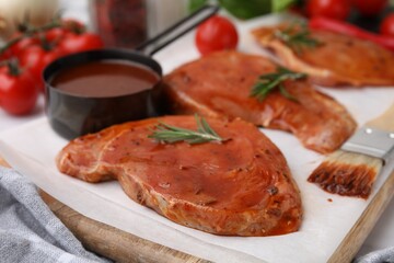 Raw marinated meat, rosemary and basting brush on table, closeup