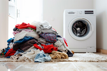 A pile of dirty clothes beside a modern washing machine. Concept of typical household chore of doing laundry.