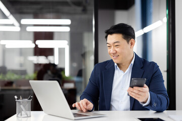 Smiling businessman using smartphone and laptop at office