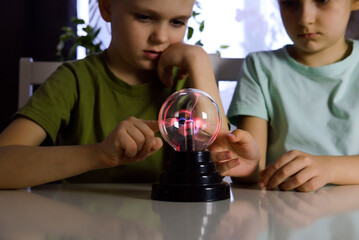 Hands holding plasma light ball. Science of light rays. Child studies touching glass sphere with his finger. Selective focus
