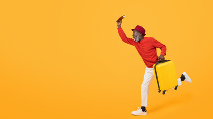 Energetic senior black man in a red sweater and hat sprinting with a yellow suitcase