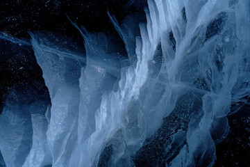 Transparent dark blue ice of frozen Baikal lake with white cracks pattern. Beautiful winter nature background.
