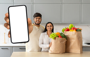 Happy young indian spouses order grocery online, showing smartphone