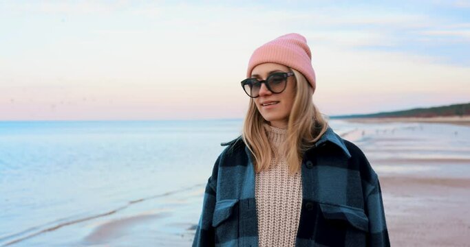 fashionable woman in coat and beanie hat enjoying walk on beach on chilly spring day