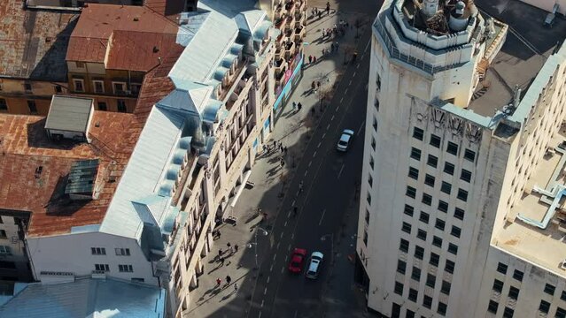 Aerial drone top view of a downtown road with moving traffic and walking people in sunlight. Bucharest, Romania