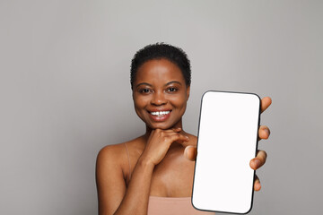 Cheerful healthy woman holding smartphone with white empty blank screen display on gray studio wall background. Happy model with phone - 763179189
