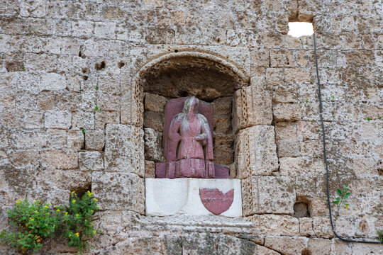 Red tinted person statue on a brick wall at the medieval city of Rhodes, Greece above the gate of Saint Anthony