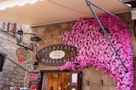 Rhodes, Greece- April 11, 2023: Gelataria - Waffleria, a sweets deserts shop in Rhodes city, Old Town market, front entrance sign and pink flower design closeup