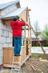 Naklejka na ściany i meble A worker builds a roof in a house while standing on a wooden ladder