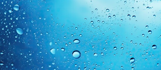 Bubbles of liquid float in the water, creating a mesmerizing display against the electric blue background. The moisture in the air forms droplets, resembling a drizzle of precipitation - obrazy, fototapety, plakaty
