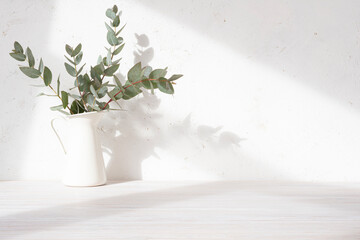 Close-up of wooden table with eucalyptus twigs in vase and light shadows