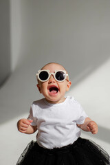 Little funny girl (1 year old) posing in sunglasses in a photo studio