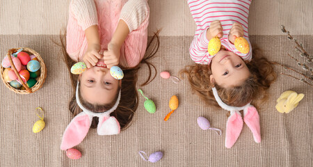 Little girls in bunny ears with Easter eggs lying at home, top view