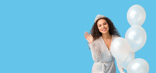 Beautiful young African-American girl in stylish dress and tiara holding balloons on light blue...