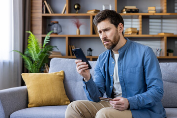 Concerned man sitting on couch looking at phone and card