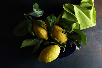 Limoni su un piatto blu; still life con vista dall’alto, composizione su fondo scuro 