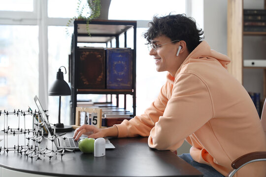 Male student studying with laptop at table in library