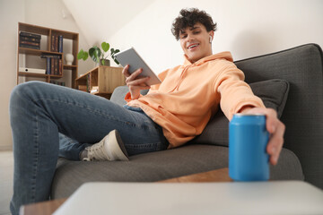 Male student with tablet computer and can of soda at home