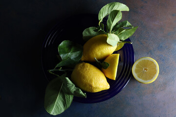 Limoni su un piatto blu; still life con vista dall’alto, composizione su fondo scuro 