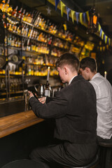 Guys spend time with alcoholic cocktails in trendy place near bar counter. Bar visitors taste alcoholic cocktails in Ukrainian pub