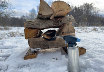 Burning bonfire in frost winter. Campfire in nature, made of dry firewood on white snow. Lighting firewood using gas burner in winter. Lighting a Fire in frost on snow. Hardwood Logs for bonfire - obrazy, fototapety, plakaty