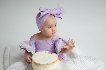 Cake crash. Photo session for baby's first birthday. Little elegant girl eats cake on a white...