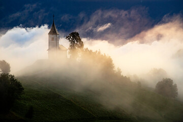 Fototapeta premium Jamnik, Slovenia - Magical foggy golden summer sunrise at Jamnik St.Primoz church.