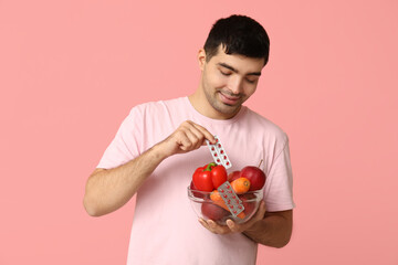 Young man with vitamin A pills and healthy food on pink background