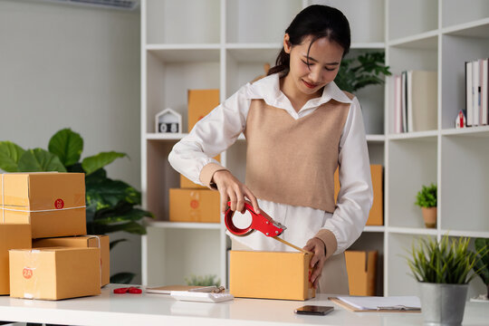 Young business entrepreneur sealing a box with tape. Preparing for shipping, Packing, online selling, e-commerce concept