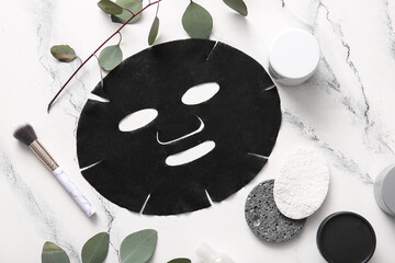 Facial sheet mask with different cosmetic products and leaves on white background