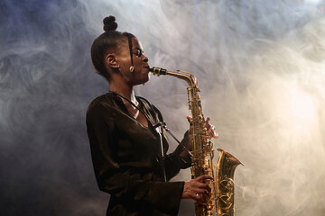Side view portrait of talented African American woman playing saxophone in jazz music club with...