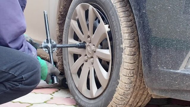 Kandra, Bashkortostan, Russia - December 01, 2023: Car mechanic removing car wheel covers using drill tool in service garage.